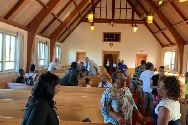 People Gathered at a traditional looking church. Light cream colored with wooden beams and seat