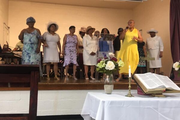Women Sunday service choir. Several women on a older wooden school style stage singing.